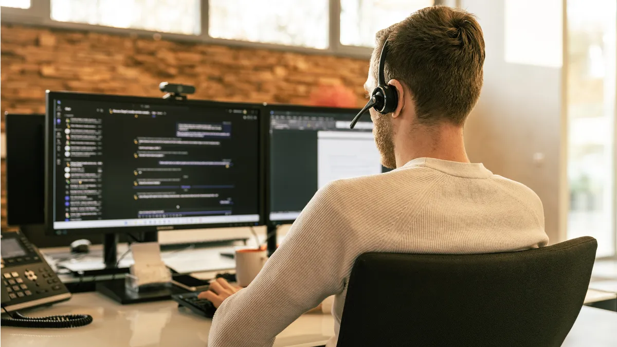 Support-Mitarbeiter mit Headset vor zwei Monitoren